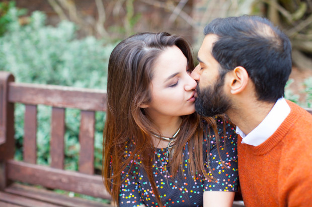 couple kissing on a bench in holland park london during their engagement session