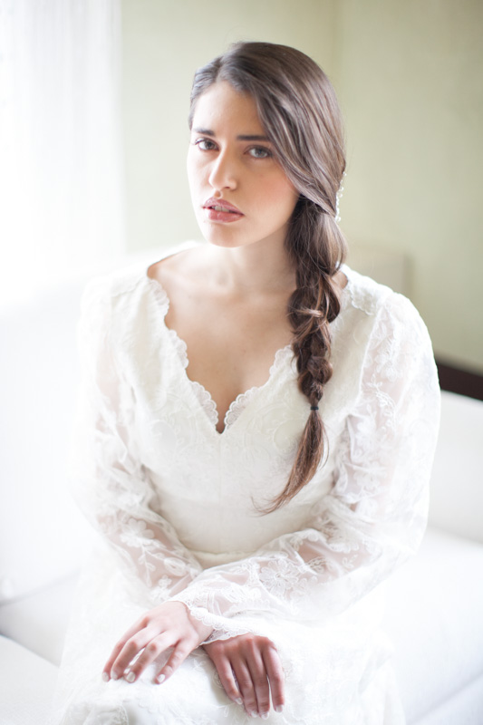 elegant wedding portrait of an italian bride with a braid in a fine art and romantic style while she is sitting on a couch in her room in italy