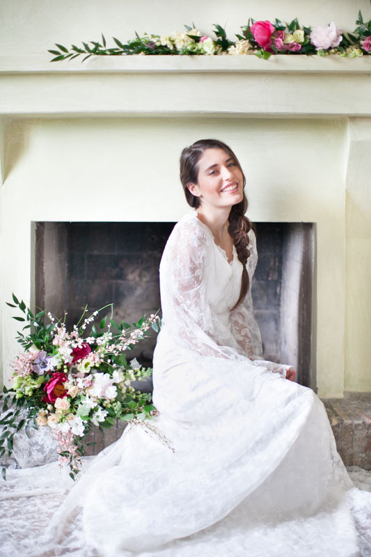 romantic portrait of an italian bride smiling with a braid sitting by a fireplace in her rustic bridal suite in italy