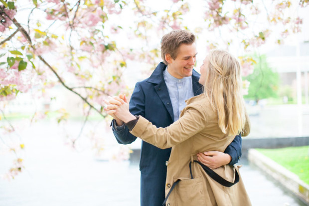 a norwegian couple dancing and smiling under a tree with pink flowers during their portrait session in bergen norway