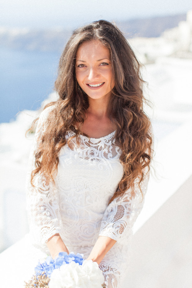 greek bride during her wedding portrait smiling and holding her white and blue bouquet at la maltese hotel in santorini