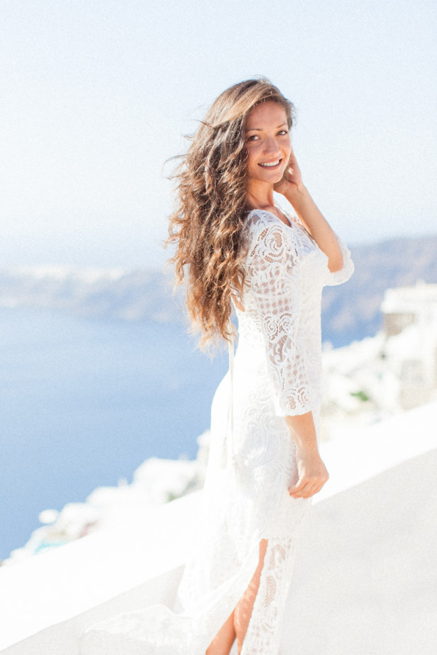a greek bride with a white dress naturally smiling during her bridal portraits at la maltese in santorini with a caldera and sea background