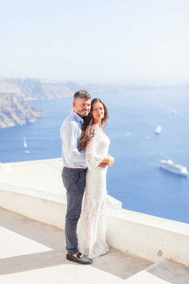 greek bride and groom holding each other during their wedding portraits in santorini greece with the sea and a boat in the background