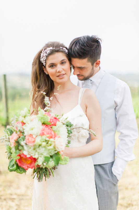 fine art and elegant wedding portrait of an italian bride and groom in the vineyards in italy in the marche region while the bride holds a bouquet with pink peonies