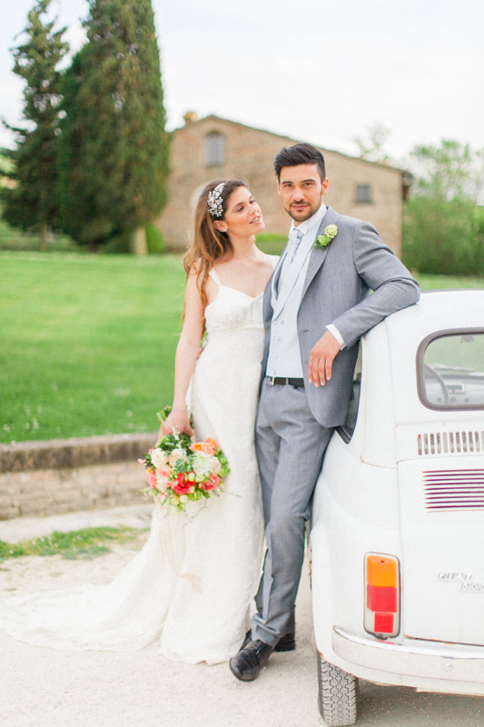 italian bride looking at her gorgeous italian husband outside their church during their wedding day in urbino in the marche region of italy next to a fiat 500