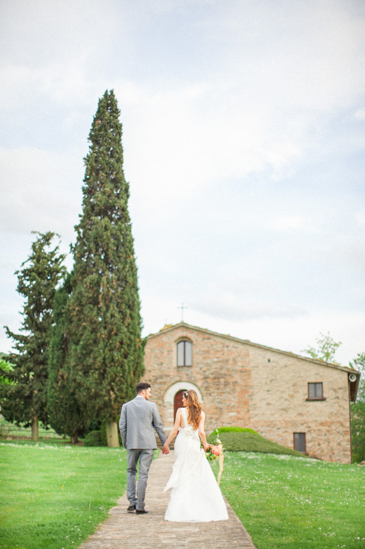 a bride and groom walking hand by hand on a path outside their church on their wedding day in italy at urbino resort