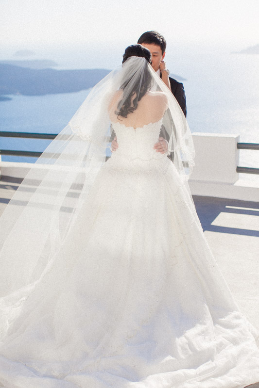 first look of a chinese bride and groom before their wedding ceremony at sun rocks hotel in santorini, the bride is from the back and the veil is blowing due to the wind