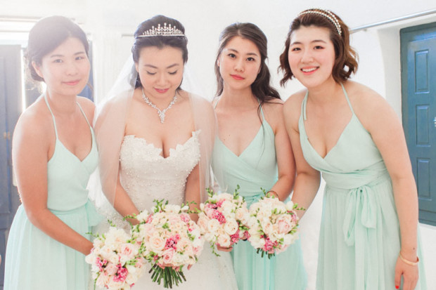 natural light portrait of a chinese bride and her bridesmaid holding the pink and white bouquets for a formal portrait on the bridal suite at sun rocks hotel in santorini