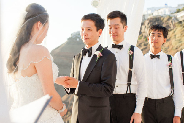 chinese wedding ceremony in santorini greece while the groom put the wedding ring on his wife while holding her hand smiling