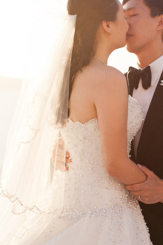 an intimate kiss of a chinese bride and groom at sunset time during their intimate wedding ceremony at the sun rocks hotel in santorini greece