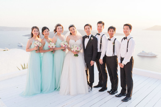 a formal portrait of a chinese bride and groom with their bridesmaids and groomsmen at the sun rocks hotel in santorini