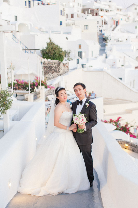 portrait of a bride and groom in a small alley in the village of firostefani in santorini greece after their intimate chinese destination wedding